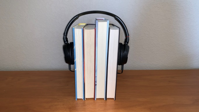 Four books with headphones set on them as if they formed a head